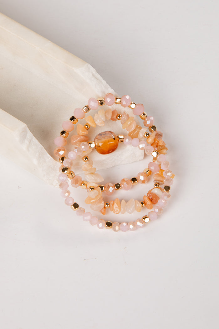 Set of beaded bracelets with peach and gold colors on a white surface