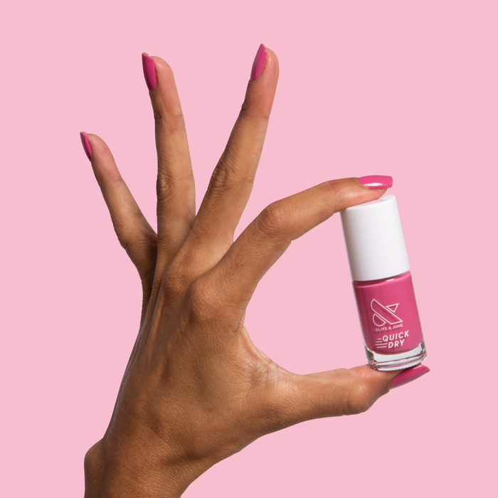 Hand holding a bottle of Prom nail polish with matching magenta nails for a quick dry at-home mani look