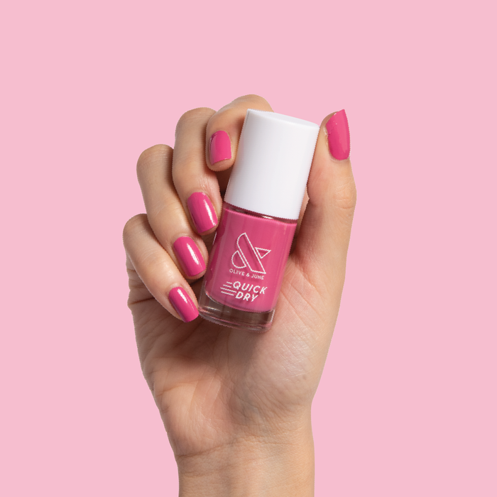 Hand holding Prom nail polish bottle with nails painted in bold magenta pink for a quick dry at-home mani look