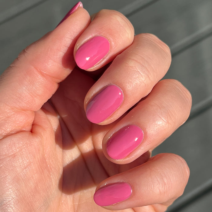 Hand with short nails painted in Prom bold magenta pink polish for a bright and polished at-home manicure look