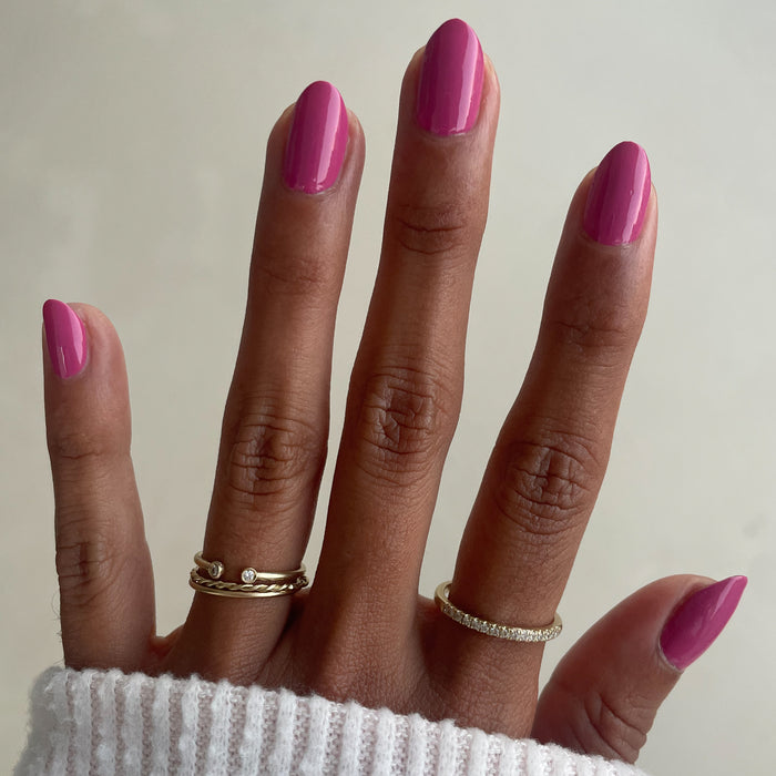Hand with almond-shaped nails painted in Prom bold magenta pink polish for a glossy at-home manicure look