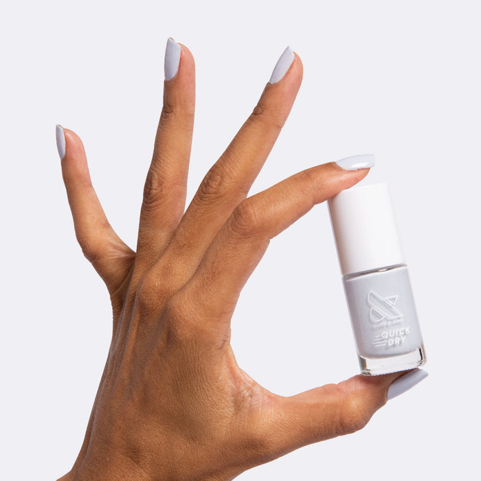 Hand holding Rink quick dry polish with nails painted in icy pastel blue for a fresh at-home manicure look