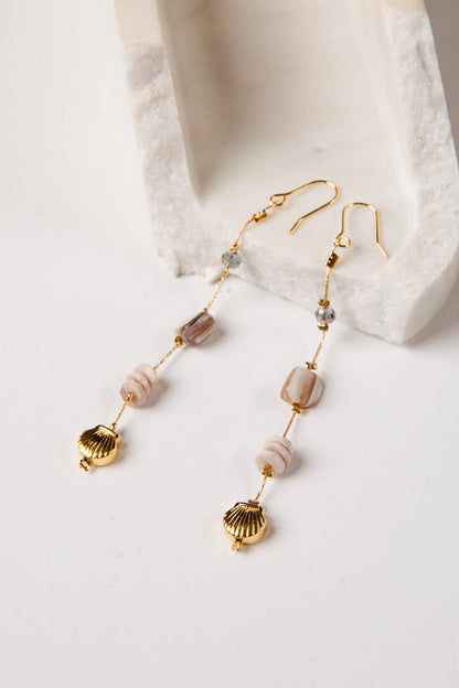 Gold earrings with shell and bead details on a white surface
