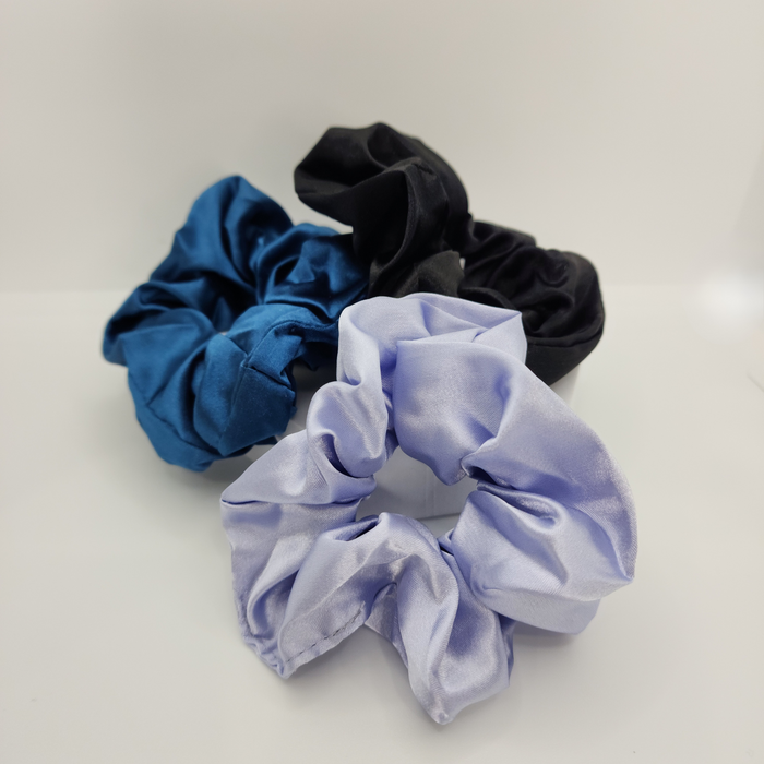 Three scrunchies in blue, black, and light purple on a white background