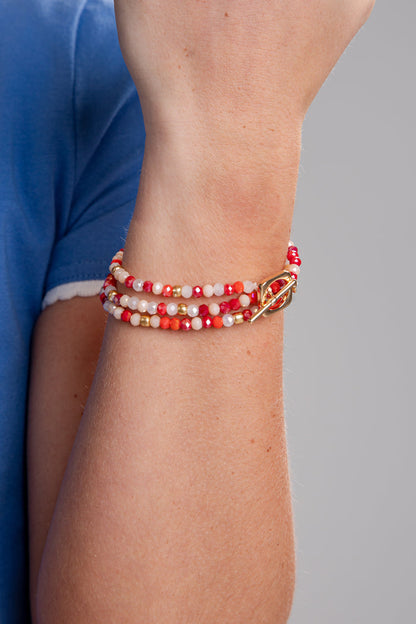Close-up of a wrist wearing a red, white, and gold beaded bracelet on a gray background.