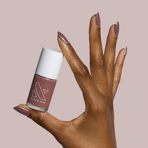 Hand with medium dark skin tone wearing Shacket polish in warm rose neutral holding matching Olive and June nail polish bottle