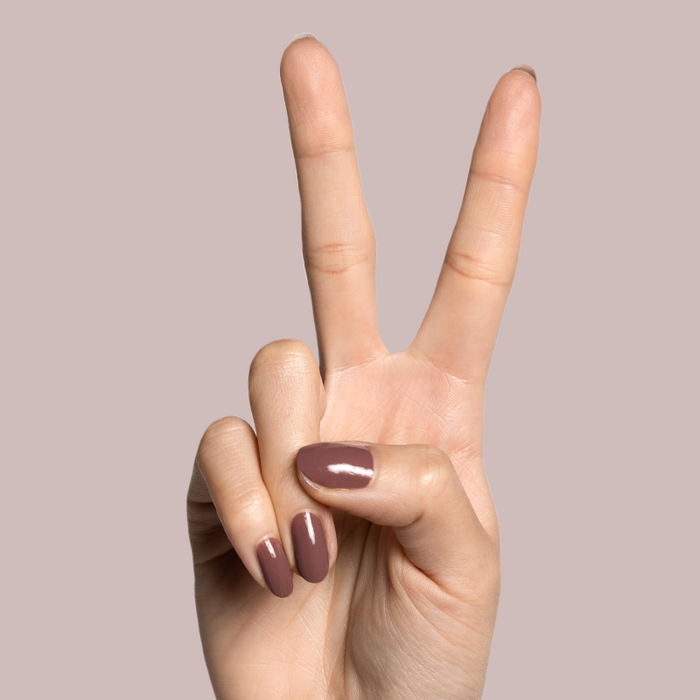 Hand with light skin tone wearing Shacket warm rose neutral gel polish for a smooth, long-lasting manicure on pink background