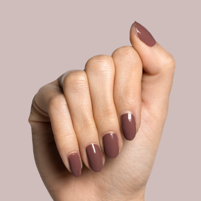 Hand with fair skin tone wearing Shacket gel polish in warm rose neutral for a smooth, long-lasting manicure on light pink background