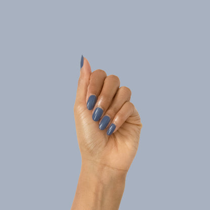 Hand with Social Studies polish in a deep sun-bleached navy shade showing a glossy manicure against a soft blue background