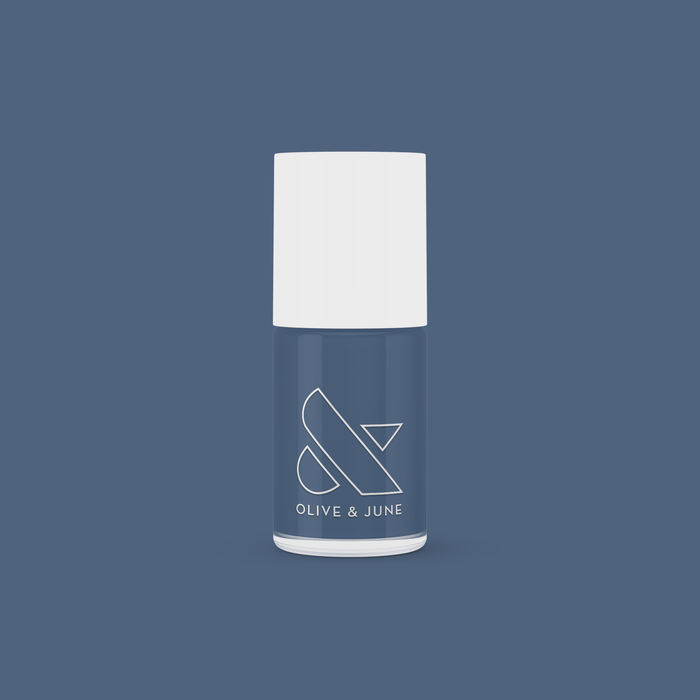 Olive and June nail polish bottle in Social Studies deep navy shade with white cap on matching blue background