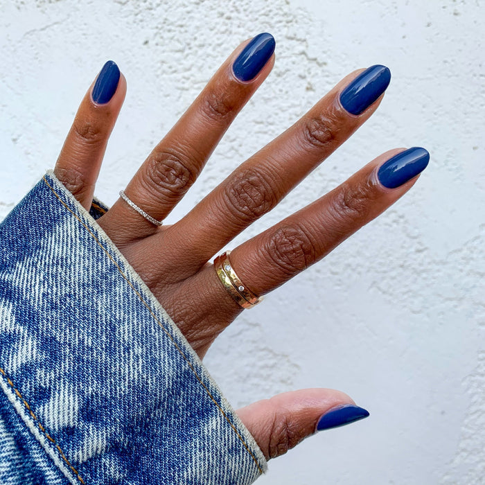 Hand with glossy Social Studies long-lasting polish in a sun-bleached deep navy shade against a light textured background