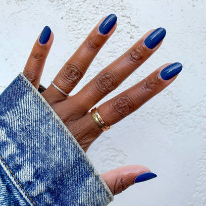 Hand with glossy Social Studies long-lasting polish in a sun-bleached deep navy shade against a light textured background