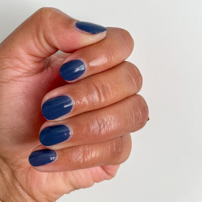 Hand showing short glossy manicure with Social Studies polish in deep sun-bleached navy on neutral background