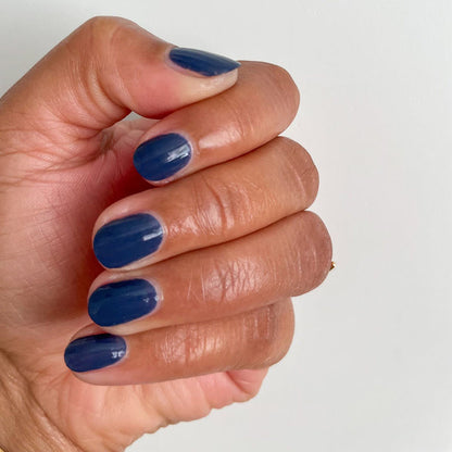 Hand showing short glossy manicure with Social Studies polish in deep sun-bleached navy on neutral background