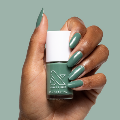 Hand with glossy nails painted in Still Life of Flowers green gel polish holding Olive and June bottle against matching green background