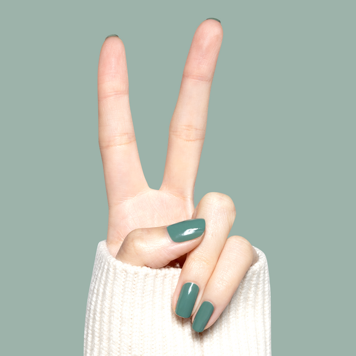 Hand with glossy nails painted Still Life of Flowers gel polish in cool mossy green showing peace sign against soft green background