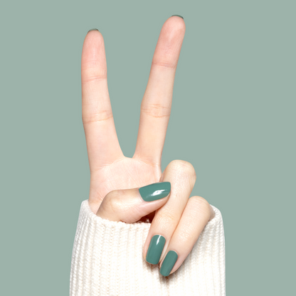 Hand with glossy nails painted Still Life of Flowers gel polish in cool mossy green showing peace sign against soft green background