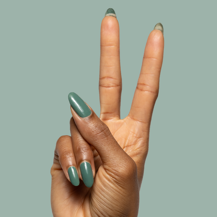 Hand with almond-shaped nails polished in Still Life of Flowers cool mossy green gel polish against muted green background