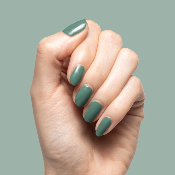 Hand with short nails painted in Still Life of Flowers gel polish in cool mossy green against muted green background
