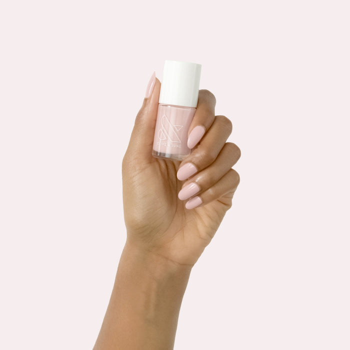 Hand holding Study Hall nail polish bottle with smooth vintage rose pink manicure on pale pink background
