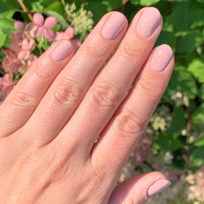 Hand with smooth manicure in Study Hall vintage rose pink polish against an outdoor floral background