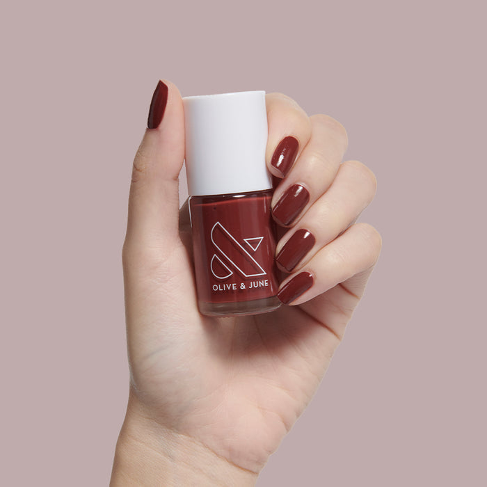 Hand holding Olive and June Team Spirit nail polish showing deep maroon manicure with long-lasting glossy finish