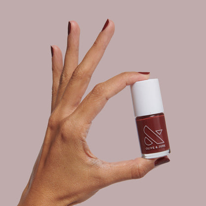 Hand holding Team Spirit nail polish bottle with polished nails in deep maroon for long-lasting manicure