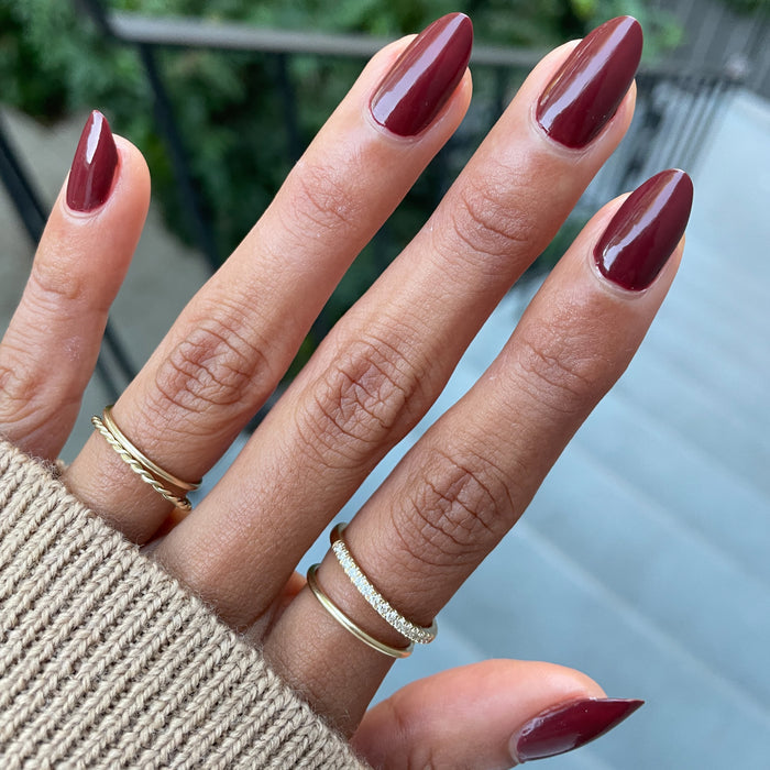 Hand with almond-shaped nails painted in deep maroon Team Spirit polish showing a glossy long-lasting manicure