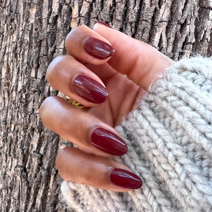 Hand with almond-shaped nails painted in deep maroon Team Spirit polish showing a glossy long-lasting manicure