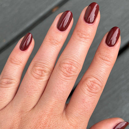 Hand with almond-shaped nails painted in shiny Team Spirit polish for a deep maroon long-lasting manicure