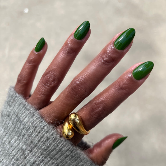 Hand with almond-shaped nails painted in Touchdown! polish, a sleek turf green for a smooth, long-lasting manicure by Olive and June