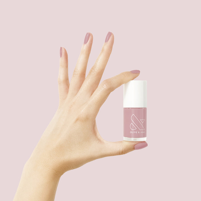 Hand with smooth mauve manicure holding World Lit nail polish bottle on a soft pink background