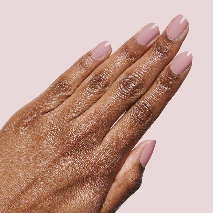 Hand with smooth mauve manicure using World Lit polish on a soft pale pink background