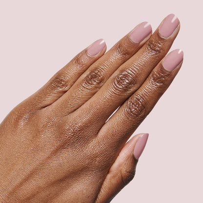 Hand with smooth mauve manicure using World Lit polish on a soft pale pink background
