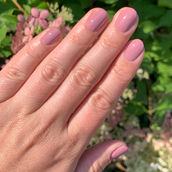 Hand with smooth mauve manicure painted with World Lit nail polish against a natural floral background